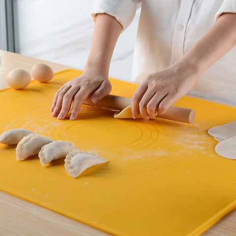 Person rolling dough on a yellow mat with dumplings and eggs nearby
