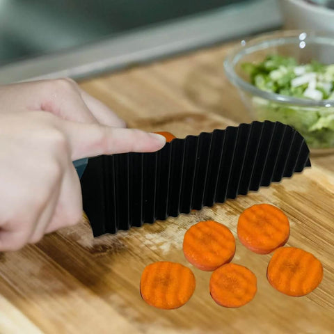 Side view of black pleated crinkle cutter with orange thumb guard, slicing five carrot coins on a wooden cutting board.