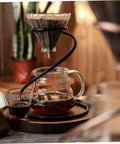 Coffee dripper holder and filter stand in use, black metal frame, brewing on a counter, ideal for home barista setups.