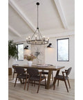 Modern dining room with wooden table, six chairs, and large black chandelier under vaulted ceiling with natural light.