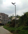 JUDYSSY Solar Floodlights mounted on a pole in a garden area with greenery and buildings in the background.