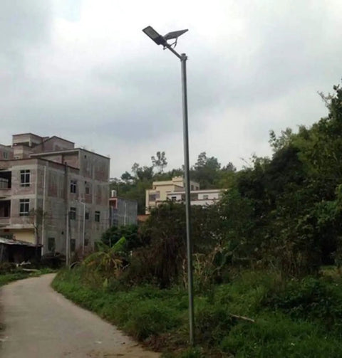 JUDYSSY Solar Floodlights mounted on a pole in a garden area with greenery and buildings in the background.