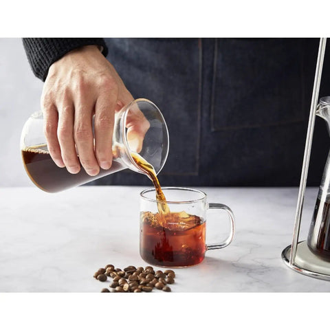 Pouring cold brew coffee from a borosilicate glass carafe into a clear cup, showcasing True Game Changer Ice Cold Brew Coffee Dripper Tower.