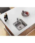 Top view of Dayton Single Bowl Drop-In Stainless Steel Bar Sink 15x15 With 2 Inch Drain Hole For Home Bars, Man Cave And Prep Areas, Quiet 300 Series Durability, Easy Drop-In Install, ADA Compliant When Properly Installed installed in a modern countertop, with wine bottles and fruit plate nearby.