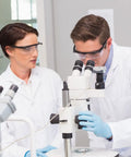 Kickass Anti Fog Safety Glasses With Legit Ansi Z87 Certification And Heavy Duty Scratch Resistant Protective Eyewear Goggles For Welding And Lab Shops worn by two researchers using a microscope in a lab.