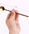 Hand holding Gold Tone 6.7 Inch Long Handle Coffee And Tea Spoon, stainless steel, mirror finish, kitchen essentials.