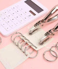 Compact Single Hole Punch Metal Circle Punch for scrapbooking and office use, 6mm hole puncher, portable craft tool on pink background with rings