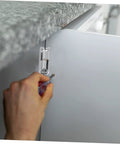 Close-up of a silver screw-on metal hinge being installed on a gray cabinet door with a screwdriver.