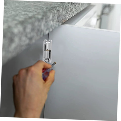 Close-up of a silver screw-on metal hinge being installed on a gray cabinet door with a screwdriver.