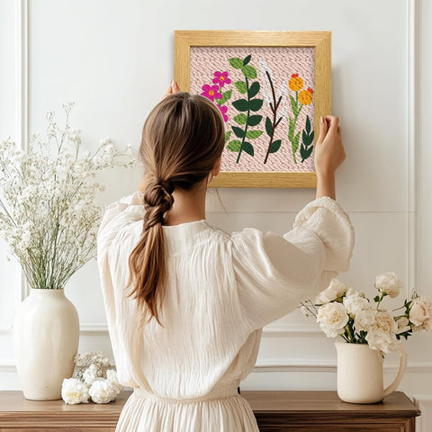 Woman hanging Wildflower Punch Needle Kit Two Pack For Beginners, Embroidery Set with frame and pre-printed fabric on wall