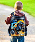 Kids backpack with blue monster-truck graphic on black background, worn by a child outdoors