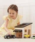 Child playing with Wooden Dollhouse Garage Set With Workbench, Lawn Mower, Bicycle And Car For Kids on carpeted floor.