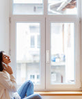 Woman seated by a modern window, enjoying a phone call in a well-lit room with a serene view outside.
