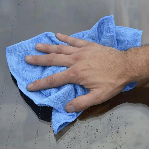 Hand using blue microfiber detailer cloth 12 pack 12 by 16 inch ultra absorbent pro grade polishing rags for car detailing