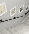 Black Wrought Iron Stair Handrail Wall Mounted Indoor Outdoor Support Bar With Kickass Ergonomic Grip Built Tough For Daily Use Senior Safety Adjustable Length Weather Resistant along stairway with artwork.