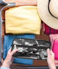 Travel Toiletry Bag For Men Women Kids Waterproof Dopp Kit Organizer held over packed suitcase with clothes and hat