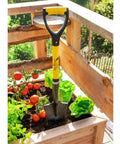 Compact 30 Inch Mini Shovel For Precision Digging in a raised planter box with tomatoes and lettuce, yellow D-Grip handle visible.