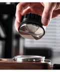 Premium Coffee Distributor And Tamper Leveler For Home Baristas held above a portafilter, showcasing its angled edges for leveling coffee grounds.