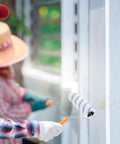 Person using Set Of 3 Pro Grade Paint Rollers For Walls And House Painting with orange handle, painting a wall outdoors.