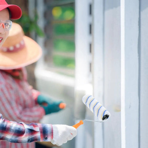 Person using Set Of 3 Pro Grade Paint Rollers For Walls And House Painting with orange handle, painting a wall outdoors.