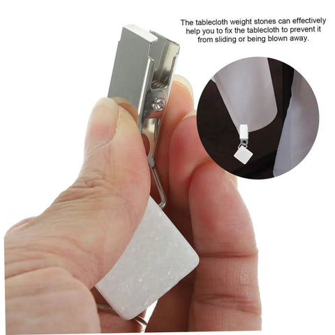 Close-up of hand holding one of six pieces gold rectangle tablecloth weights clips for outdoor tables, showing clip mechanism.
