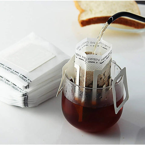 Grab And Go Portable Disposable Drip Coffee Bags With Hanging Ear brewing over a glass mug, stack of single serve filter papers nearby.