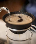 Top Shelf Reusable Ceramic Pour Over Dripper With Hella Fine Pores filtering coffee into a glass, showcasing its black ceramic design.