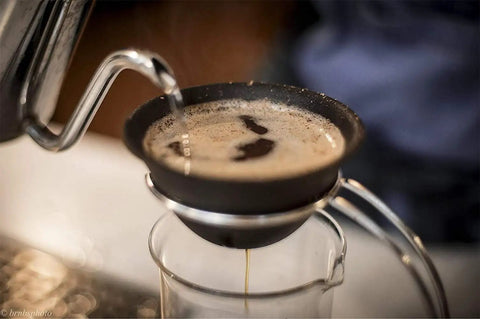 Top Shelf Reusable Ceramic Pour Over Dripper With Hella Fine Pores filtering coffee into a glass, showcasing its black ceramic design.
