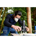 Dremel 335-01 plunger router attachment in use on wood outdoors by a person wearing safety goggles and mask.