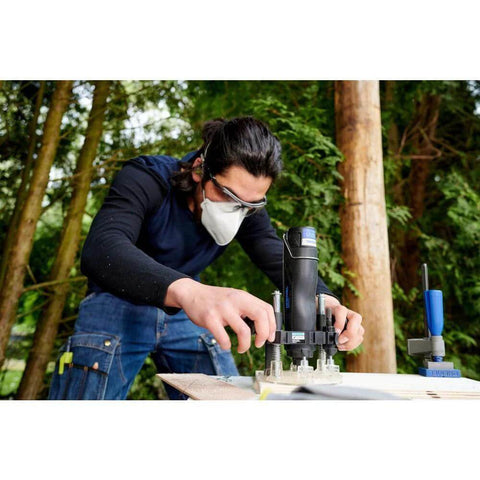 Dremel 335-01 plunger router attachment in use on wood outdoors by a person wearing safety goggles and mask.