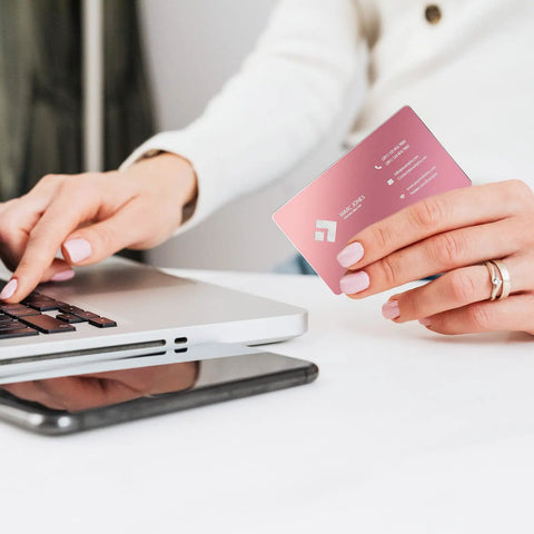 Person holding Colorful Aluminum Metal Business Card Blank near laptop, pink card, 3.38 x 2.12 inches, for laser engraving.