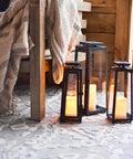 Outdoor Solar Lanterns With Flameless Candles Two Pack 11 Inch Tall Black Metal Glass Lanterns for patio, set on textured rug.