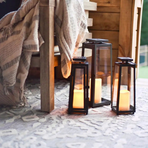 Outdoor Solar Lanterns With Flameless Candles Two Pack 11 Inch Tall Black Metal Glass Lanterns for patio, set on textured rug.