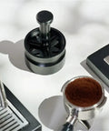 Killer Precision Rotary WDT Tool For Espresso Portafilter on a light surface next to a coffee portafilter with grounds.