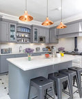 Modern kitchen with grey cabinets, white countertops, copper pendant lights, and black stools under island