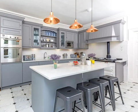 Modern kitchen with grey cabinets, white countertops, copper pendant lights, and black stools under island