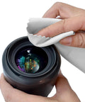 Close-up of hands wiping a camera lens with a white microfiber cloth