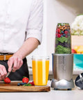 Person preparing fruit with blender and 32 Oz Cup Replacement Parts Kit With 2 Flip Top Lids, 2 Rubber Gaskets, And 2 Replacement Blades