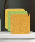 Sparkling cardstock sheets in gold, green, and yellow displayed on a shelf, ideal for die cuts and scrapbooking projects.