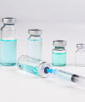 Angled front view of five 5ml glass injection vials with metal caps and blue liquid, syringe nearby.