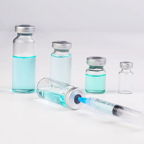 Angled front view of five 5ml glass injection vials with metal caps and blue liquid, syringe nearby.