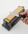Tri Hone Stone Sharpening System Three Way Honing With 1000 Grit Fine Arkansas Stone, 800 Grit Medium, 300 Grit Coarse Stone, hand holding knife