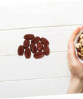 Realistic Walnut Miniature Pecans Set Ten Pieces For DIY Decor And Fake Food Props on a white tabletop with a hand holding mixed nuts.