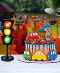 Traffic Light Table Lamp For Kids With Color Changing LEDs next to a colorful car-themed cake in an outdoor setting.