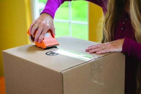 Person using Ultra Tough Packing Tape With Dispenser For Moving And Shipping, Clear 2.83 Inch By 35 Yard, 3.4 Mil Thick on a box