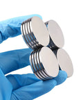 MIKEDE neodymium disc magnets with double-sided adhesive, 1.26 in diameter, four magnets held by a gloved hand
