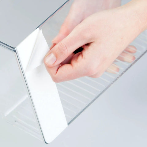 Hands peeling adhesive from clear plastic wall mount organizer for kitchen bathroom office garage and craft room versatile wall mounted storage box to hold spices meds gadgets toiletries and small items keeps your pad tidy three point five by eleven by six point five inches.