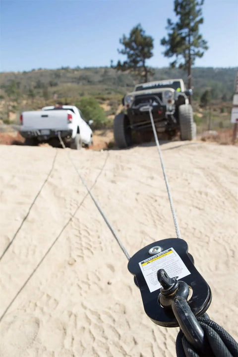 Beefy Heavy Duty Snatch Block For Winches 17,600 Lb Capacity Universal Fit Seven Thirty Two To Three Eighths Inch Cable Greasable Bearing Black Powder Coat Off Road Recovery Tool used with winch cables on a sandy trail