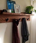 Wall-mounted shelf with matte black stainless steel towel hooks holding towels, surrounded by decor items including a plant.