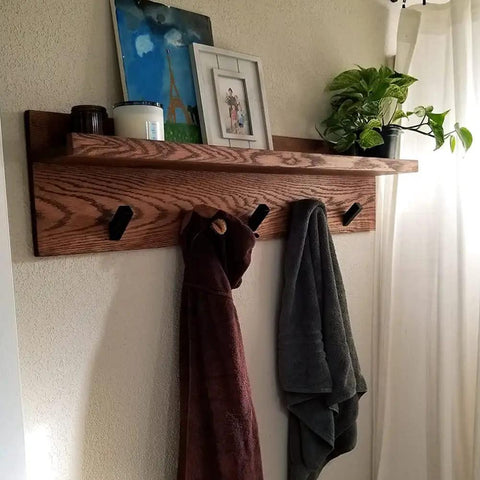 Wall-mounted shelf with matte black stainless steel towel hooks holding towels, surrounded by decor items including a plant.